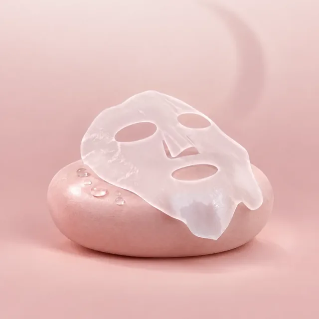 La lámina de gel de la Bio Collagen Mask, translúcida y con huecos para los ojos, la nariz y la boca, sobre una piedra rosada.